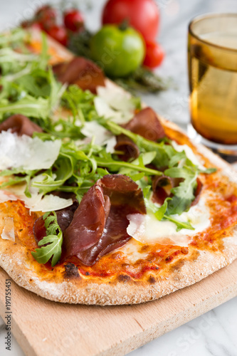 Gourmet Salami, parmesan and rocket pizza served on a rustic wooden board.