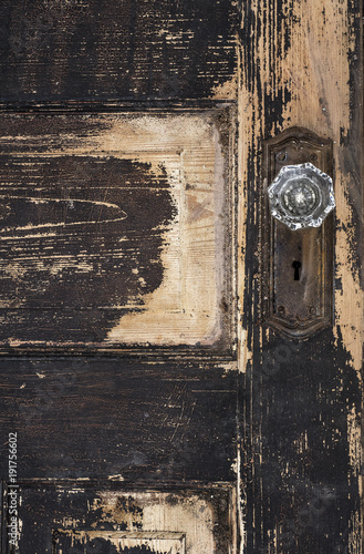 Old weathered antique beat-up wood panel door with chipped peeling paint and glass crystal doorknob and rusted plate