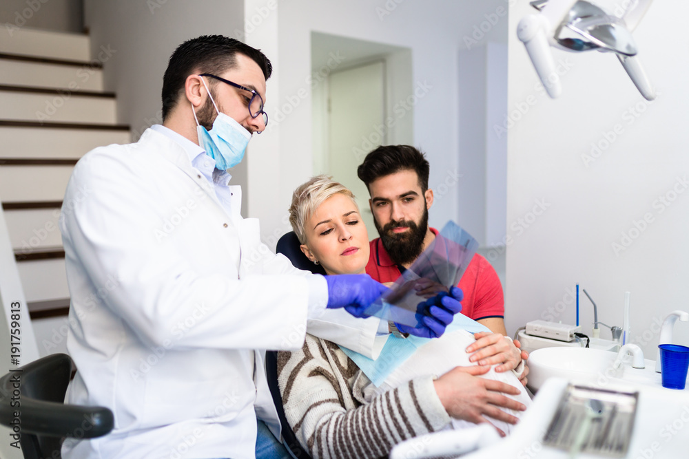 Obraz premium Attractive bearded man with his pregnant wife having medical treatment in dental office