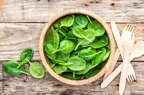 Fresh baby spinach leaves in bowl on wooden background