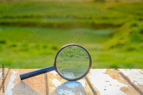 Magnifying glass standing on wooen table against green background