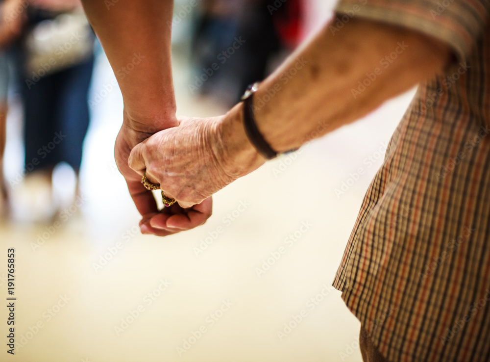wrinkled elderly woman's hand holding to young man's hand, walking in shopping mall. Family Relation, Health, Help, Support, Insurance concept.