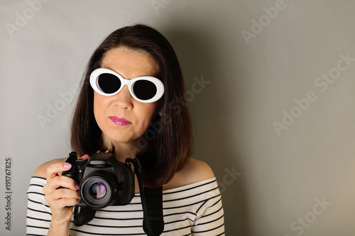 Woman in a white striped top and white sunglasses holding a camera.