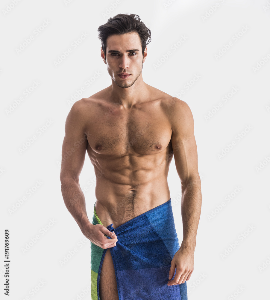 Fototapeta premium Portrait of naked handsome young man with languishing look covering crotch with a towel, against light background