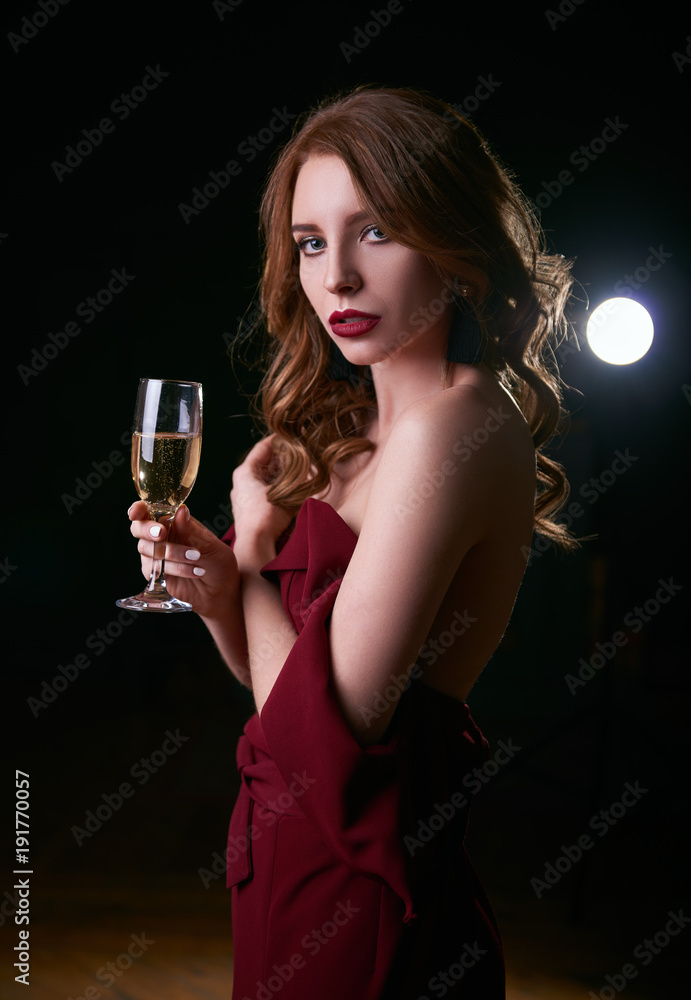 Portrait of seductive beautiful young woman in lowered red dress  with a glass of champagne in hand