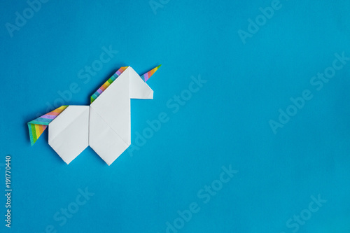 Handmade white trendy geometrical polygonal paper origami unicorn on blue background. Empty space. Horizontal poster, postcard, banner template.