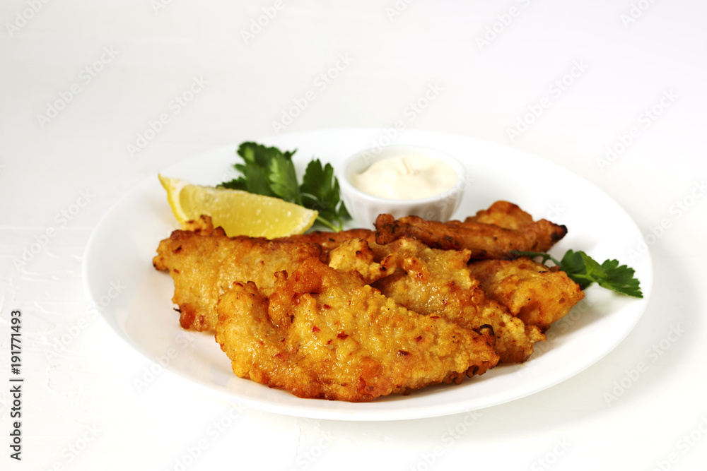 Golden batter deep fried fish fillets, served on white plate with sauce and lemon Golden batter deep fried fish fillets, served on white plate with sauce and lemon