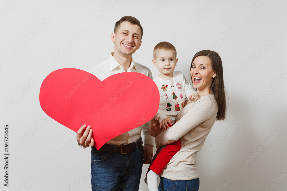 Joyful smiling young man, woman holding, hugging little cute child boy with big red heart isolated on white background. Father, mother, little kid son. Parenthood, family, parents and children concept