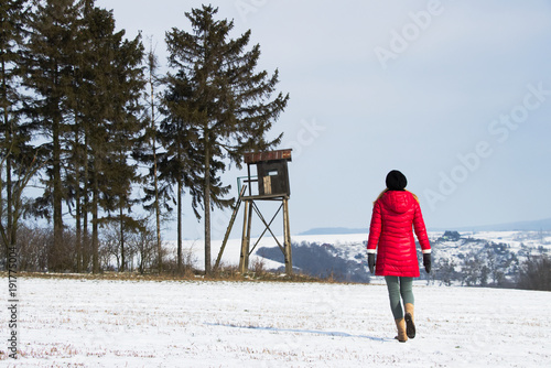 Hiking woman is walking to a hunting tower in countryside at winter