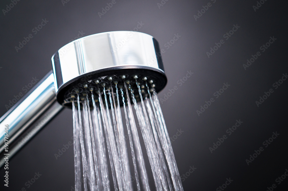 Close up of shower head against dark black background. Water running from faucet in modern bathroom. Close up of shower head against dark black background. Water running from faucet in modern bathroom.
