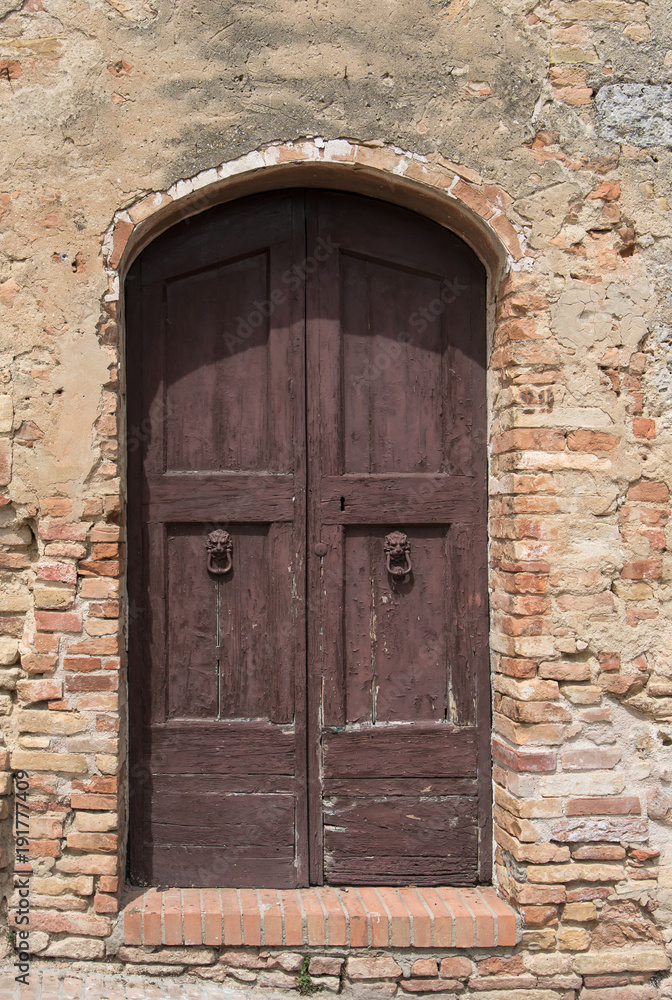 Old wooden door in sunlight set in brick wall