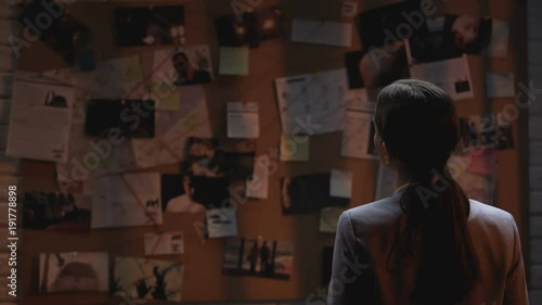 Lady private agent looking at crime investigation board, drinking cup of coffee