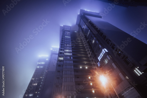 Low angle view on modern illuminated buildings at foggy night