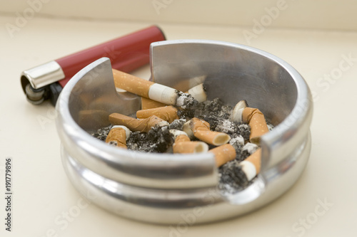 Ashtray full of extinguished cigarette butts with one lit