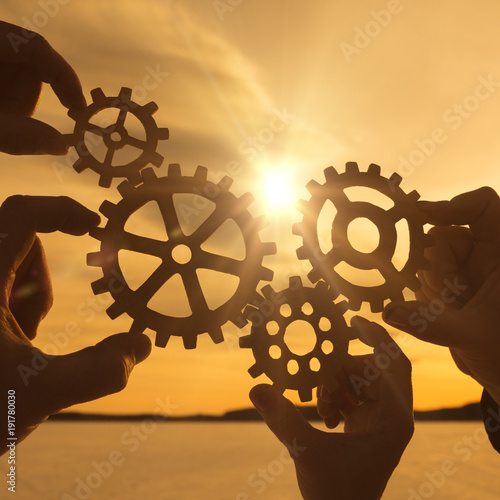 Four hands collect the gear from the gears of the details of the puzzles. against the background of sunlight. Concept business idea. Teamwork. Close-up