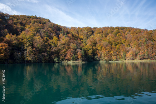 Turquoise colored water contrasting the fall colors of the trees in Plitvice Lakes National Park. It is a cloudy autumn day.