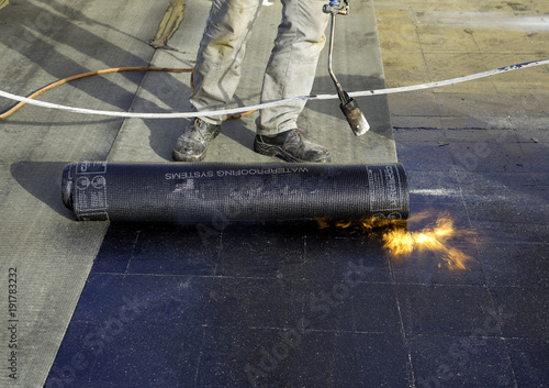Canvas-taulu Worker preparing part of bitumen roofing felt roll for melting by gas heater tor
