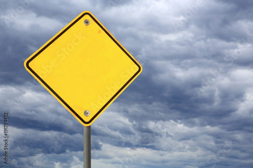 empty yellow road warning sign against a dark stormy sky 