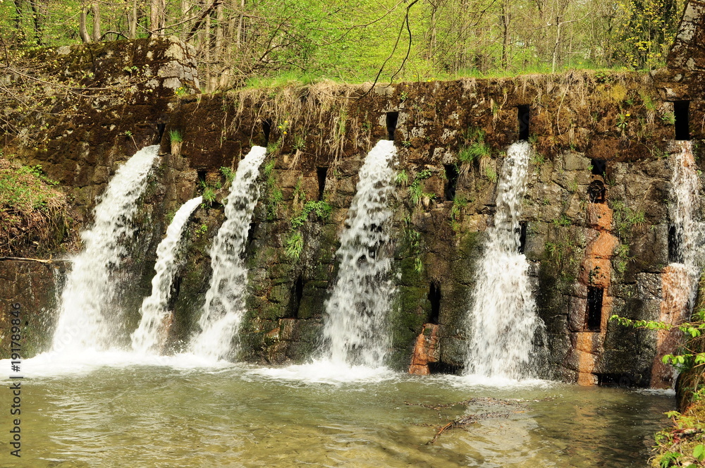 Fototapeta premium Wodospad, woda wypływająca z ściany. Trzy małe wodospady w lesie. Zdjęcie ostre ze zbliżeniem.