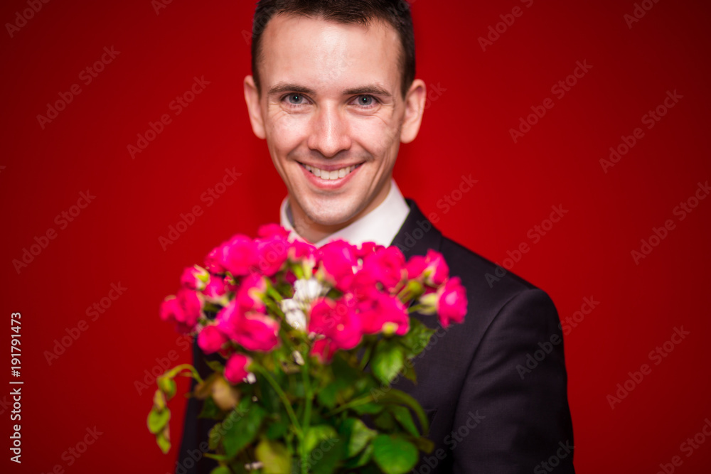 Stylish man in suit holding a bouquet of flowers with red background Stylish man in suit holding a bouquet of flowers with red background