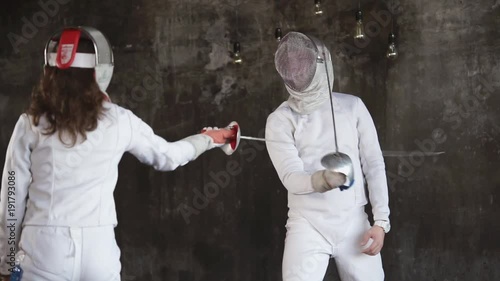 Two begginers are practicing defence moves with a fence sword in studio. Man and woman are fighting. photo