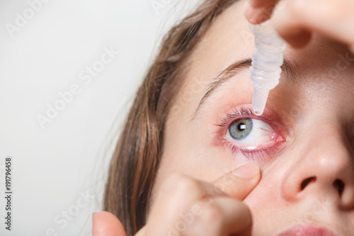 Female puts eye drop in her inflamated red eye, suffers from conjuctivitis, isolated on white. Woman applies eye drops. Eye treatment and health concept