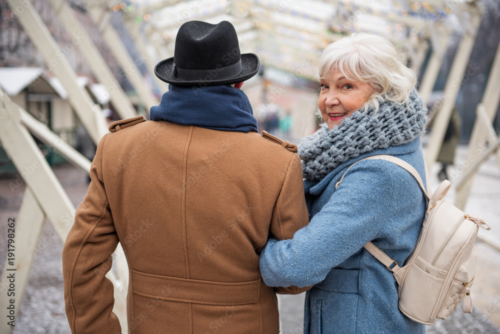 Portrait of happy old woman looking back with interest while walking arm in arm with man. She is laughing Portrait of happy old woman looking back with interest while walking arm in arm with man. She is laughing