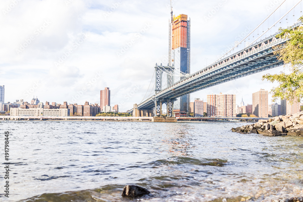 Rocky pebble beach shore water in east river with view of NYC New York City cityscape skyline and bridge, nobody in Brooklyn
