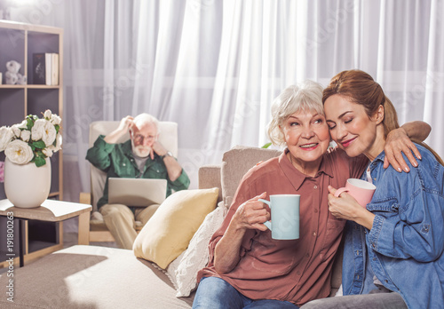 Portrait of happy grandmother hugging young woman. They tasting mug of beverage. Family concept