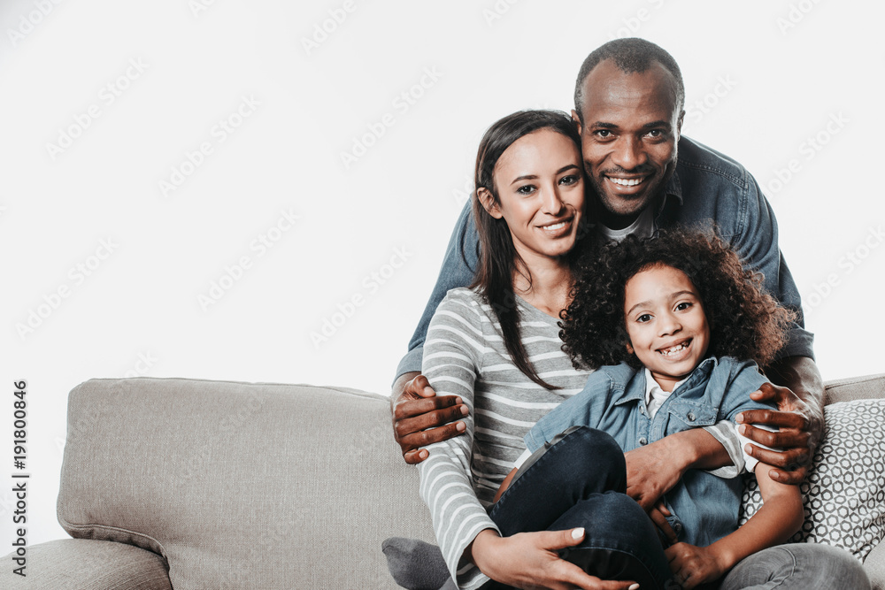 Portrait of african family looking at camera with joy while reposing on sofa with coziness. Copy space in left side. Isolated on background