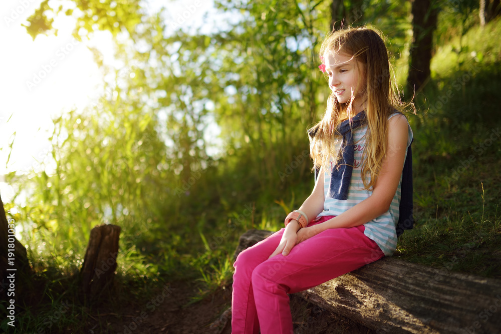 Cute little girl sitting by the lake enjoying beautiful sunset view. Child exploring nature. Cute little girl sitting by the lake enjoying beautiful sunset view. Child exploring nature.