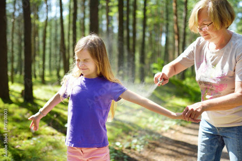 Middle age woman applying insect repellent to her granddaughter before forest hike beautiful summer day. Protecting children from biting insects at summer.