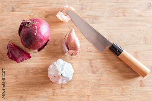 Red onion, shallot, and garlic on a wood cutting board with the japanese knife photo