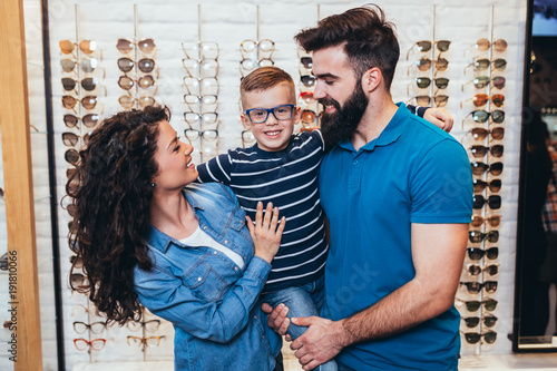 Konstfotografi Happy mother and father choosing eyeglasses frame for their son in optical store