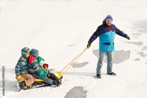 Happy boys enjoy sledding. Yellow children's sled. The kid is riding a sleigh. Children playing outdoors in the snow. In winter, children ride on a frozen lake. Outdoor fun for family winter vacations