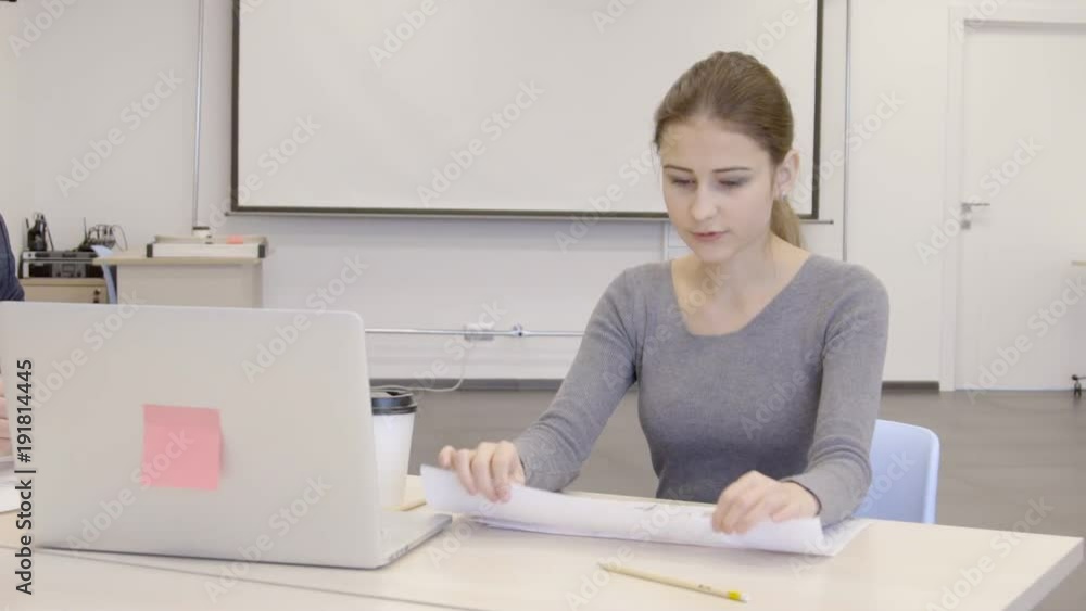 Businesswoman is tearing paper with currency exchange rate graphs on in the office. Female boss is sitting at the wooden table with laptop, cup of coffee and documents in conference rom and analyzing Businesswoman is tearing paper with currency exchange rate graphs on in the office. Female boss is sitting at the wooden table with laptop, cup of coffee and documents in conference rom and analyzing