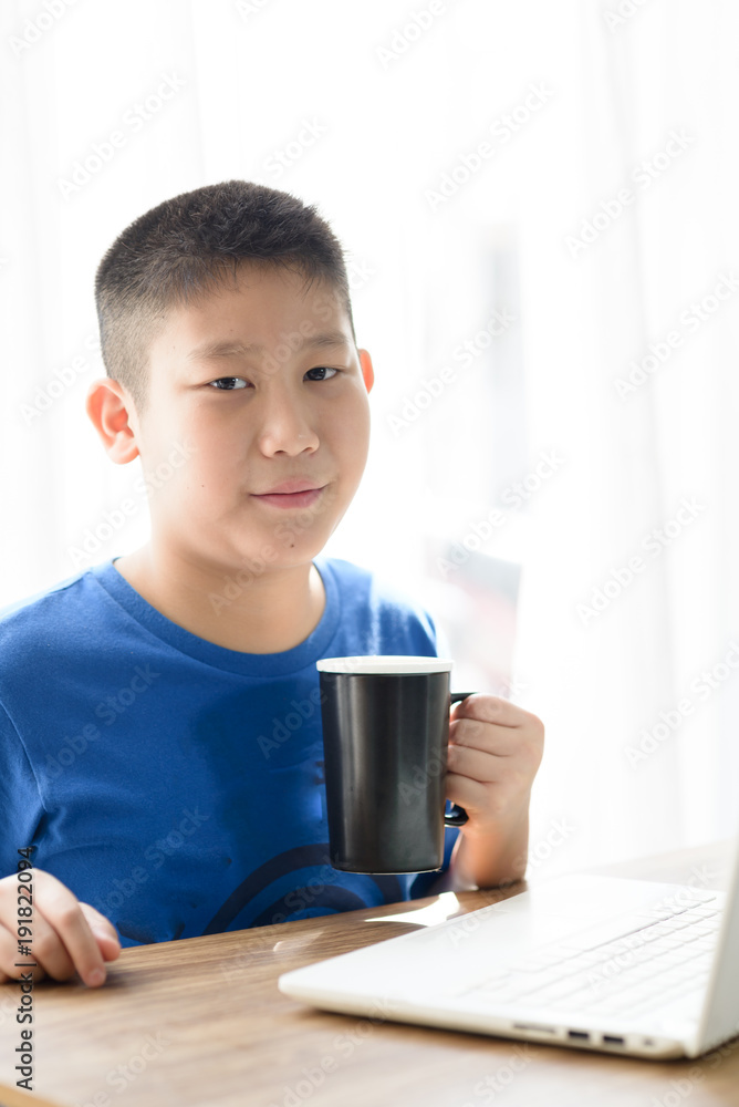 Happy Asian boy holding black cup while using tablet at home. Happy Asian boy holding black cup while using tablet at home.