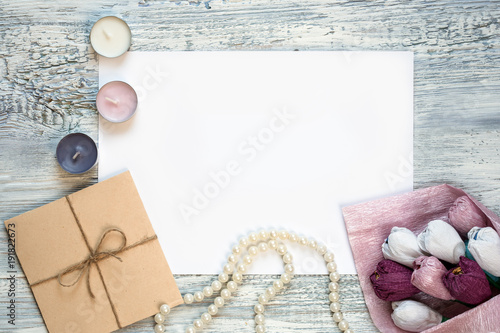 blank white greeting card and envelope with candles beads and flowers over rustic table with copy space. mock up