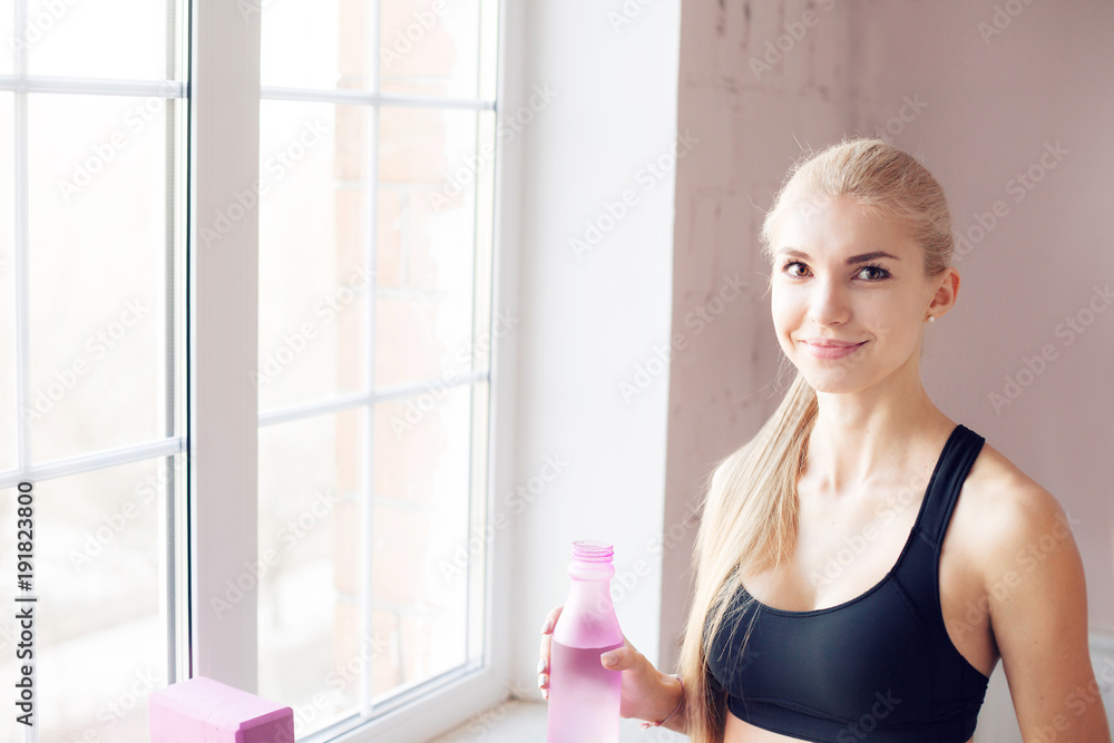 home fitness. drink clean water from a bottle. Lovely young blonde girl. near the window home fitness. drink clean water from a bottle. Lovely young blonde girl. near the window