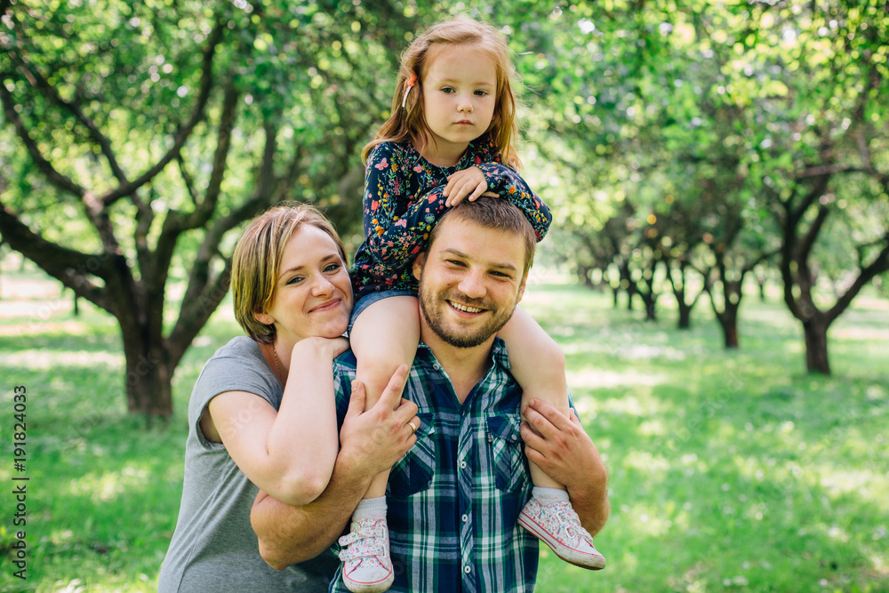 Fototapeta premium Cute young happy family having fun in the park. Little girl with parents outdoors. Mother father and daughter.