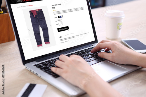 People buying blue navy jeans on ecommerce website with smart phone, credit card and coffee on wooden desk