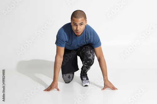 Ready, steady, go. Horizontal isolated studio shot of attractive concentrated young African American male runner with muscular arms dressed in trendy sports clothes preparing to run marathon or sprint