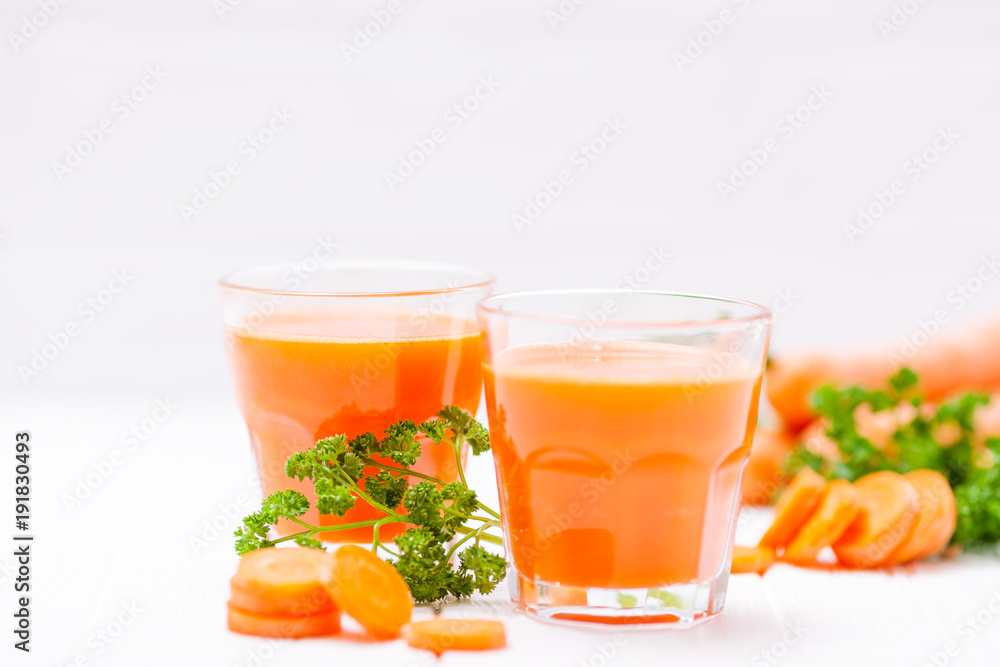 Carrot juice in beautiful glasses, cut orange vegetables and green parsley on white wooden background. Fresh orange drink. Close up photography. Selective focus. Horizontal banner Carrot juice in beautiful glasses, cut orange vegetables and green parsley on white wooden background. Fresh orange drink. Close up photography. Selective focus. Horizontal banner