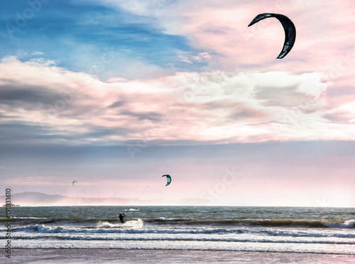 Kite surfers glide on the waves of the Atlantic ocean. Extreme sport concept. Active leisure landscape