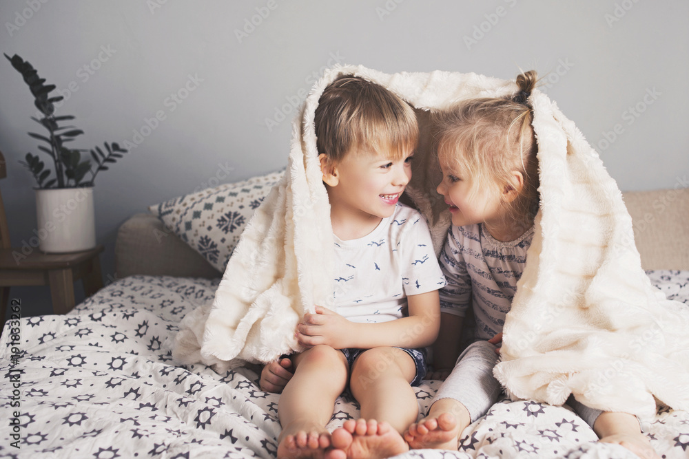 Two pretty kids embrace under blanket - obrazy, fototapety, plakaty 