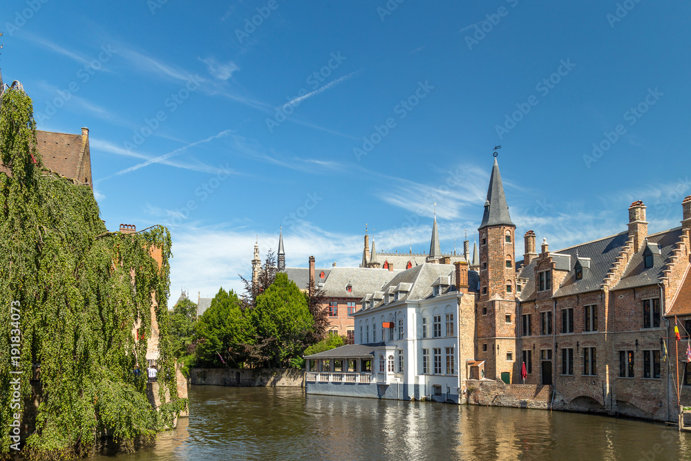 The Rozenhoedkaai canal in Bruges with the belfry in the background. Typical view of Bruges (Brugge), Belgium with red brick houses with triangle shaped roofs and canals.