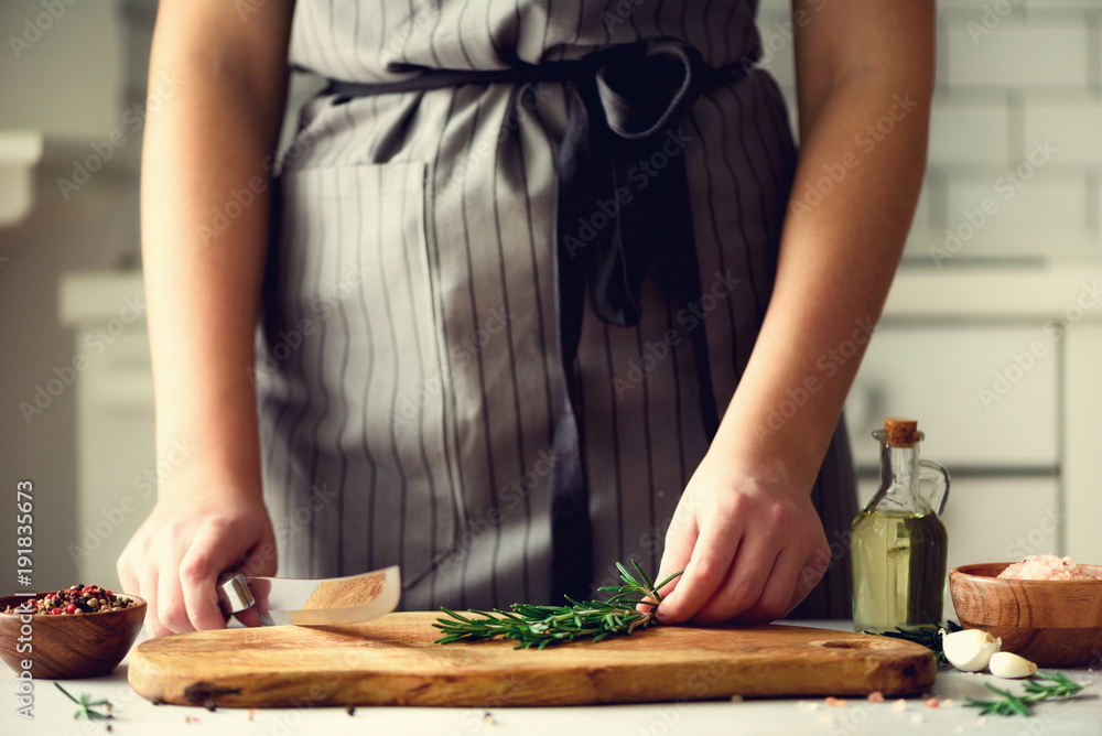 Woman hands cutting fresh green rosemary on wood chopping board in white kitchen, interior. Copy space. Homemade food conceplt, healthy recipe. Take me to work