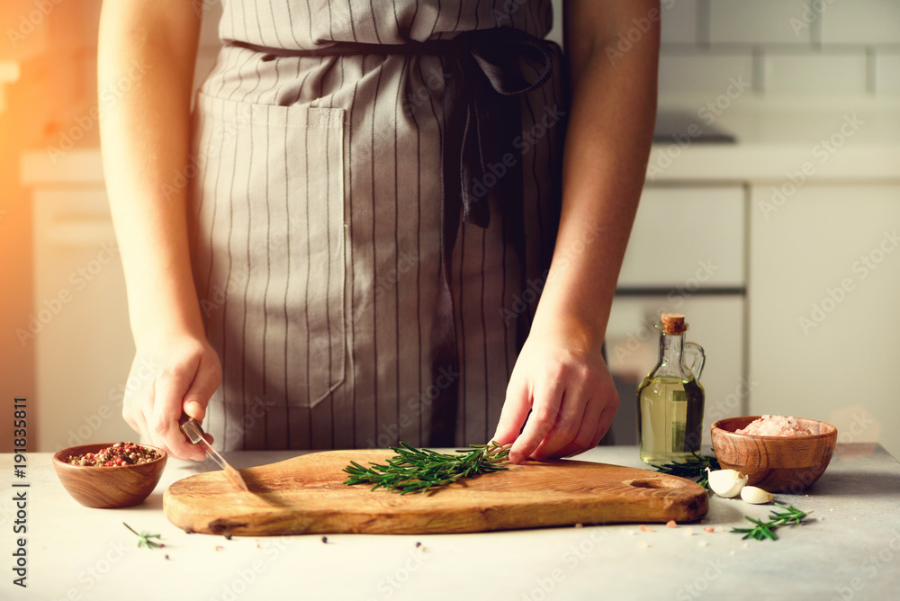Woman hands cutting fresh green rosemary on wood chopping board in white kitchen, interior. Copy space. Homemade food conceplt, healthy recipe. Take me to work