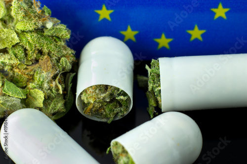 Medical Pills of Cannabis - marijuana  flowers inside tablets with European Union flag on the black mirror background.