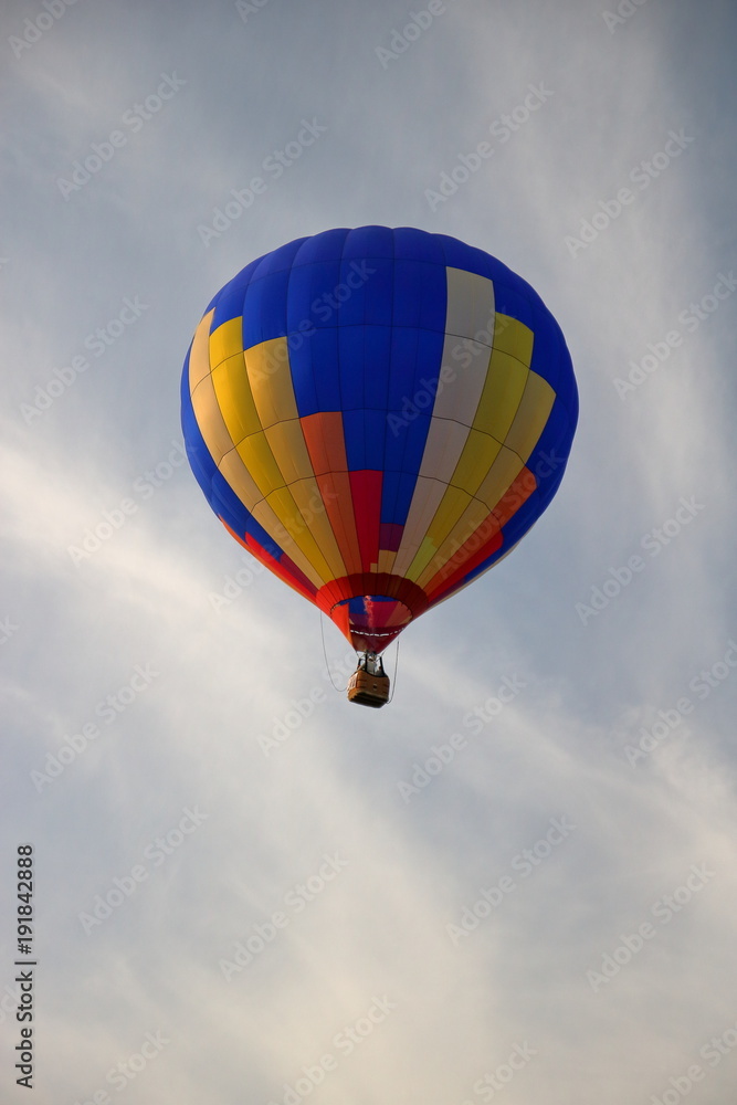 Kolorowy balon unosi się w powietrzu, z podwieszonym koszem, na tle szarobłękitnego nieba Kolorowy balon unosi się w powietrzu, z podwieszonym koszem, na tle szarobłękitnego nieba